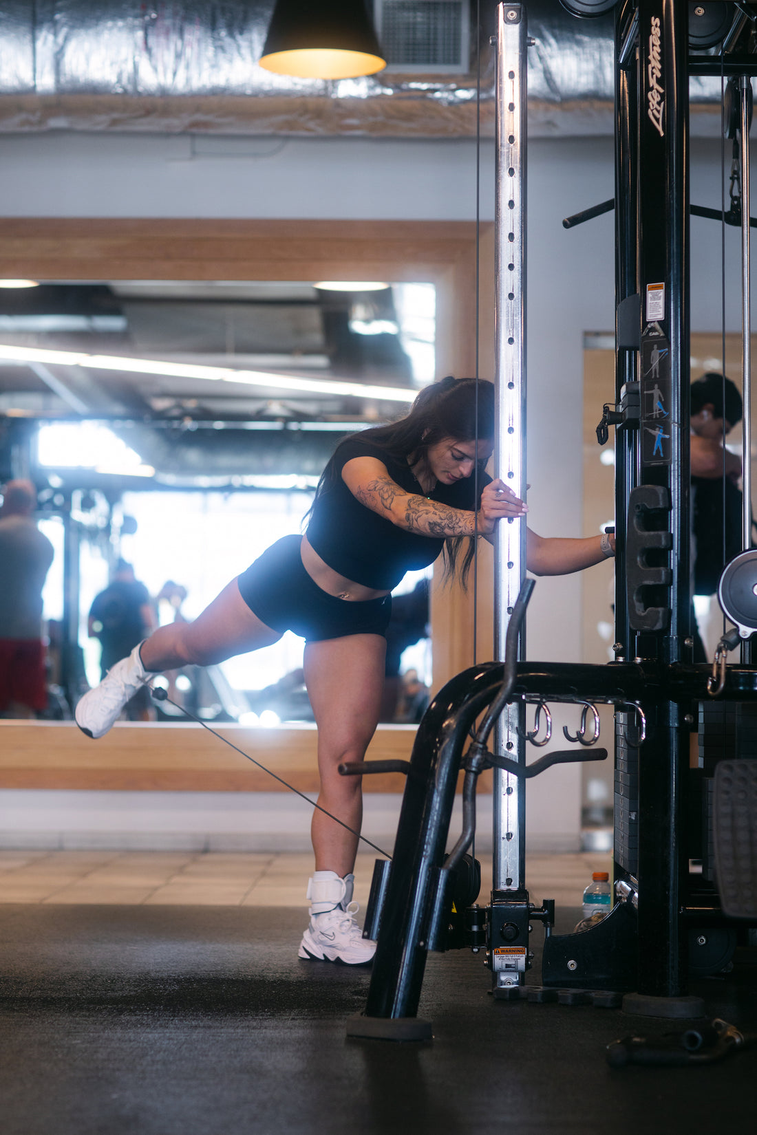 woman doing cable leg kickbacks with uppper ankle straps